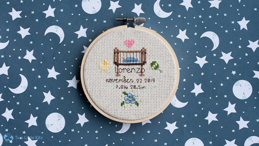 Cross-stitch finished piece: a baby in a cot/crib with birth details