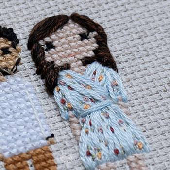 Cross-stitch & embroidery piece depicting a woman in a floral, flowy dress with loose, wavy brown hair.