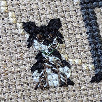 Cross-stitch piece depicting a black, white and brown dog sitting next to its owner.
