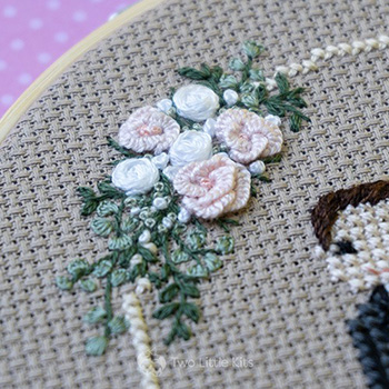 Embroidery piece depicting a bouquet of flowers on a circle shape with delicate leaves and pastel pinks.