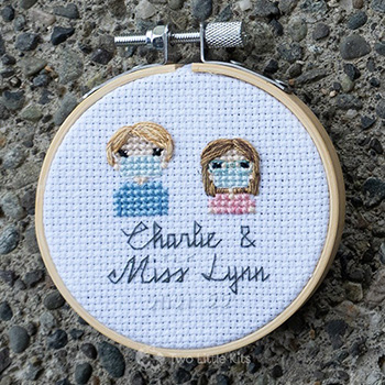 Miss Lynn and Charlie, both cross-stitched wearing face masks in a stitch people style.