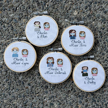 Five 3in embroidery hoops of crosss-stitched pieces that all include one adult and the same little girl across them all as bust shots. They are stitch people portraits and all say 'Charlie &' and then her therapist's name with the date '2021-22' faintly underneath. They are all laid flat on a stony floor.
