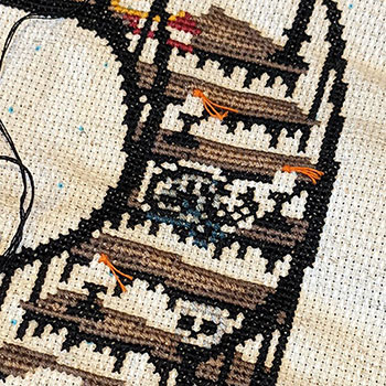 A close-up photograph of a work-in-progress cross-stitch depicting a curled up ghost-cat on a flight of stairs. Part of The Haunted Library stitch-along