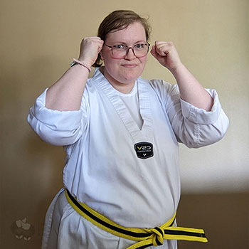 A photo of Kate in a white Gi wearing a yellow belt with a black stripe. She's standing in a fighting stance