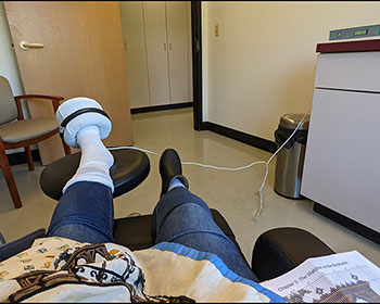 A weird angled photo of Kate's legs elevated with a bone stimulation device on her left foot.