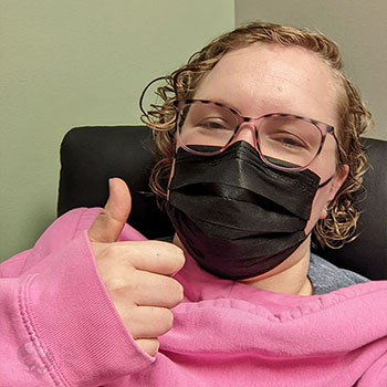 Kate, looking groggy, wearing a face mask and giving the camera a thumbs up