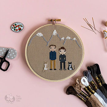 A stitch people piece depicting two people and two cats with an outline of a snow-tipped mountain in the background.