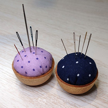 Two little pun cushions with a dozen-or-so needles in them both: one is purple with dots and the other is navy blue with dots.