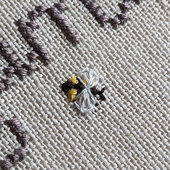 A macro photograph of a tiny cross-stitch and backstitched bee.