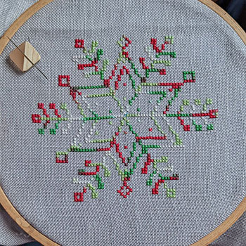 A work-in-progress of a variegated snowflake stitched on linen cloth
