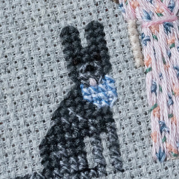 A cross-stitched, black and grey dog with a blue and white bandana around its neck.