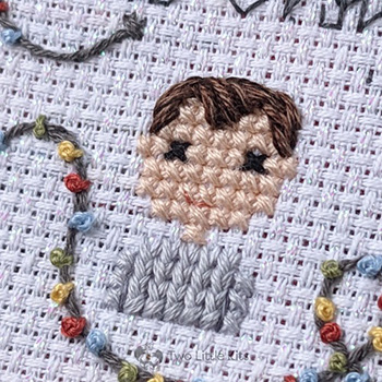 A close-up photo of a cross-stitched boy with brown hair that has a distinct cowlick in it. He is wearing a grey sweater that has been stitched in a way that looks knitted.