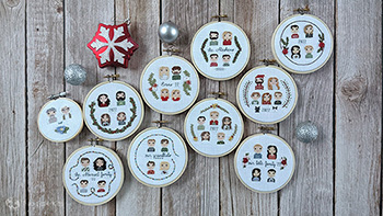 All 10 cross-stitch and hand embroidered Christmas ornaments laid out flat on a faux wood background. 9 of them are in a 4