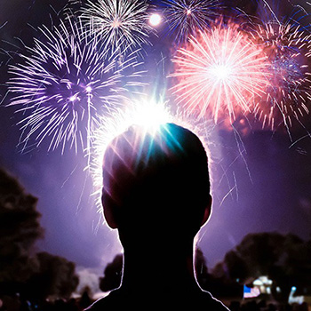 A picture of a person facing away from the camera, looking up at a night sky full of fireworks.