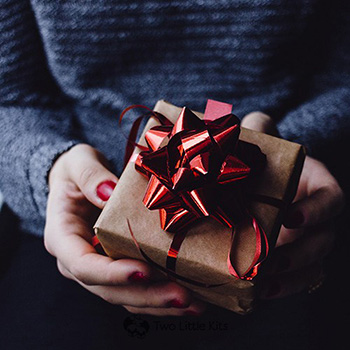 A close-up photo of a woman wearing red nail polish holding a beautifully decorated, square gift.
