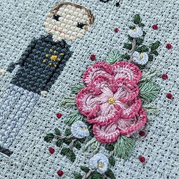 A close-up photograph of hand embroidered florals and a cross-stitched man