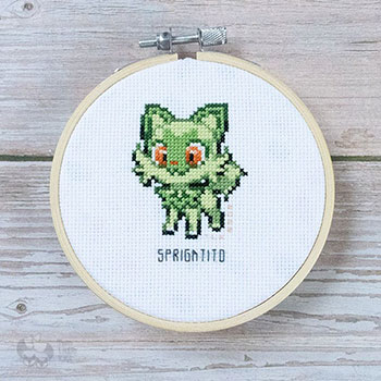 A photograph of a cross-stitched 'Sprigatito' - a grass cat from the current versions of Pokémon.