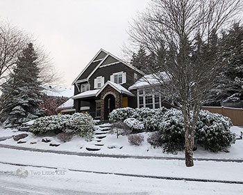 A photograph of fresh snowfall outside a dark-coloured house.