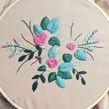 A half-finished embroidery piece with pink flowers and greenery.