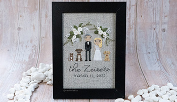 A framed hand stitched, stitch people wedding portrait. It has a bride and groom, plus two dogs and one cat. It says 'The Zeisers' with a future date and hand embroidered florals above it all.