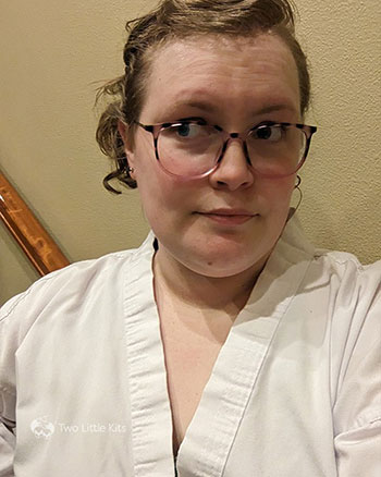 A selfie photograph of Kate in a white martial arts uniform. Her hair is roughly pinned back and she's smirking while looking away.