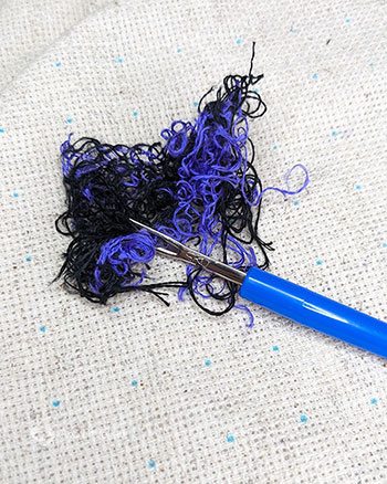 A messy bundle of black and bright purple floss with a seam ripper laying on top of it.