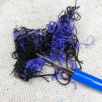 A messy bundle of black and bright purple floss with a seam ripper laying on top of it.