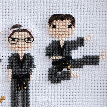 Two cross-stitched people -one man, one woman- in black martial arts uniforms with black belts.